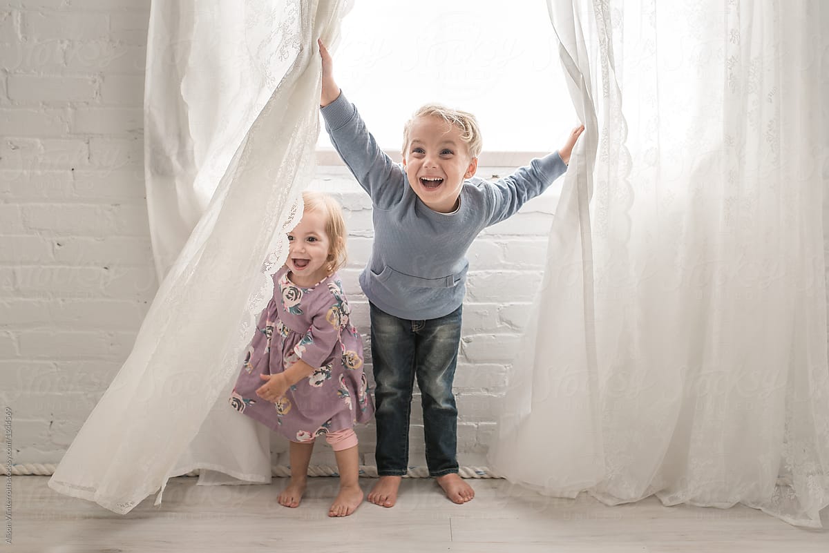 Two Children Playing Peek A Boo In The Curtains