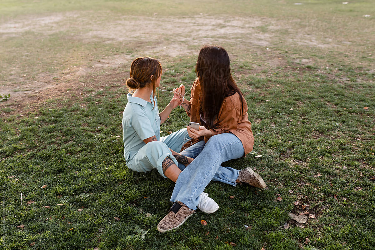 Lesbian Couple Holds Hands and Listens to Music While Hanging Out in a Park