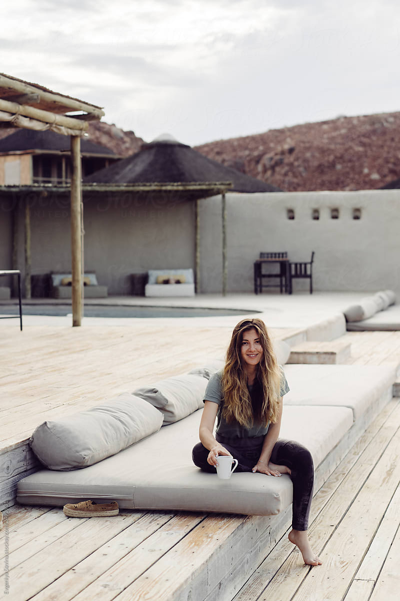A girl sitting on a wooden deck with a cup of coffee in the desert