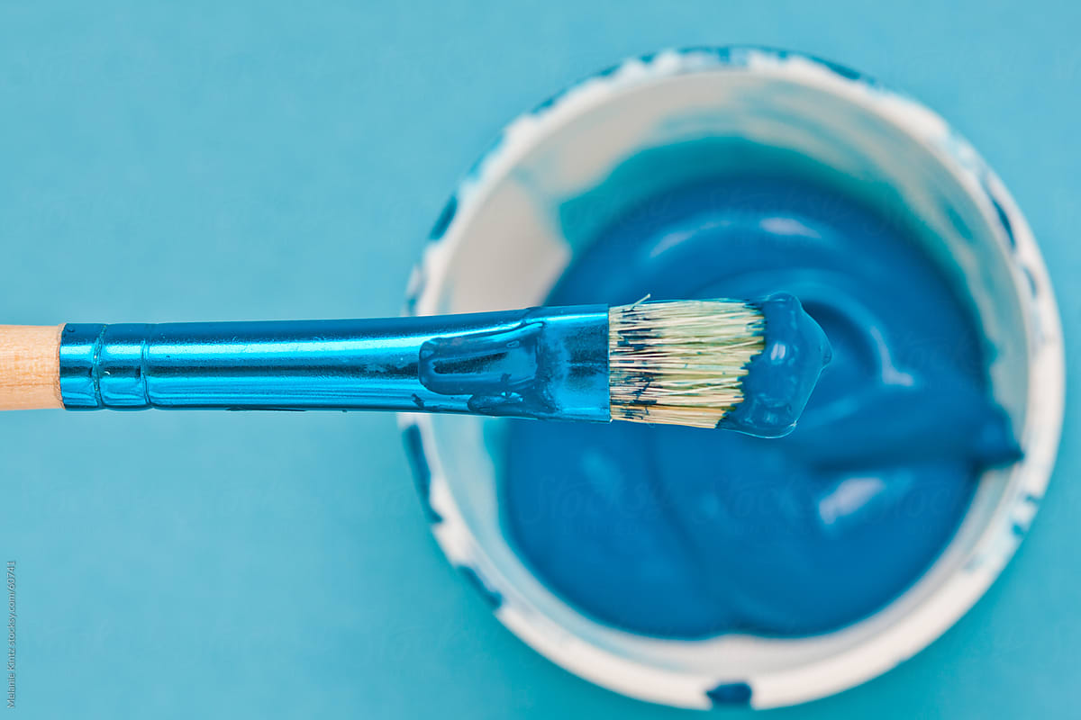 paintbrush with teal paint on bristles over paint container