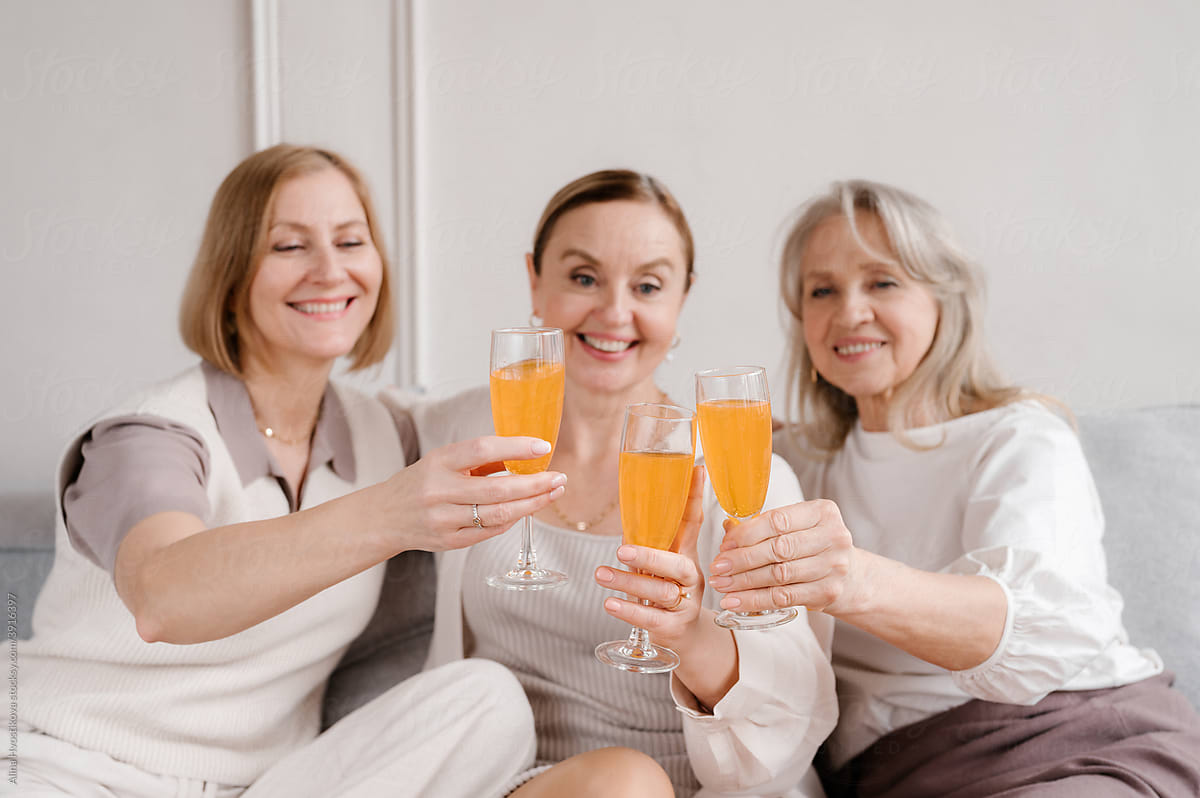 Company of smiling women clinking glasses during celebration at home