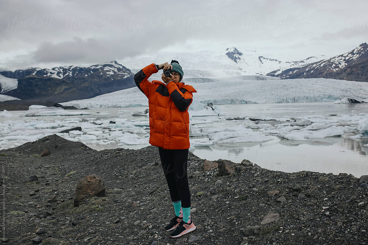 Female Explorer in red jacket taking photo on Glacier Lagoon, Iceland