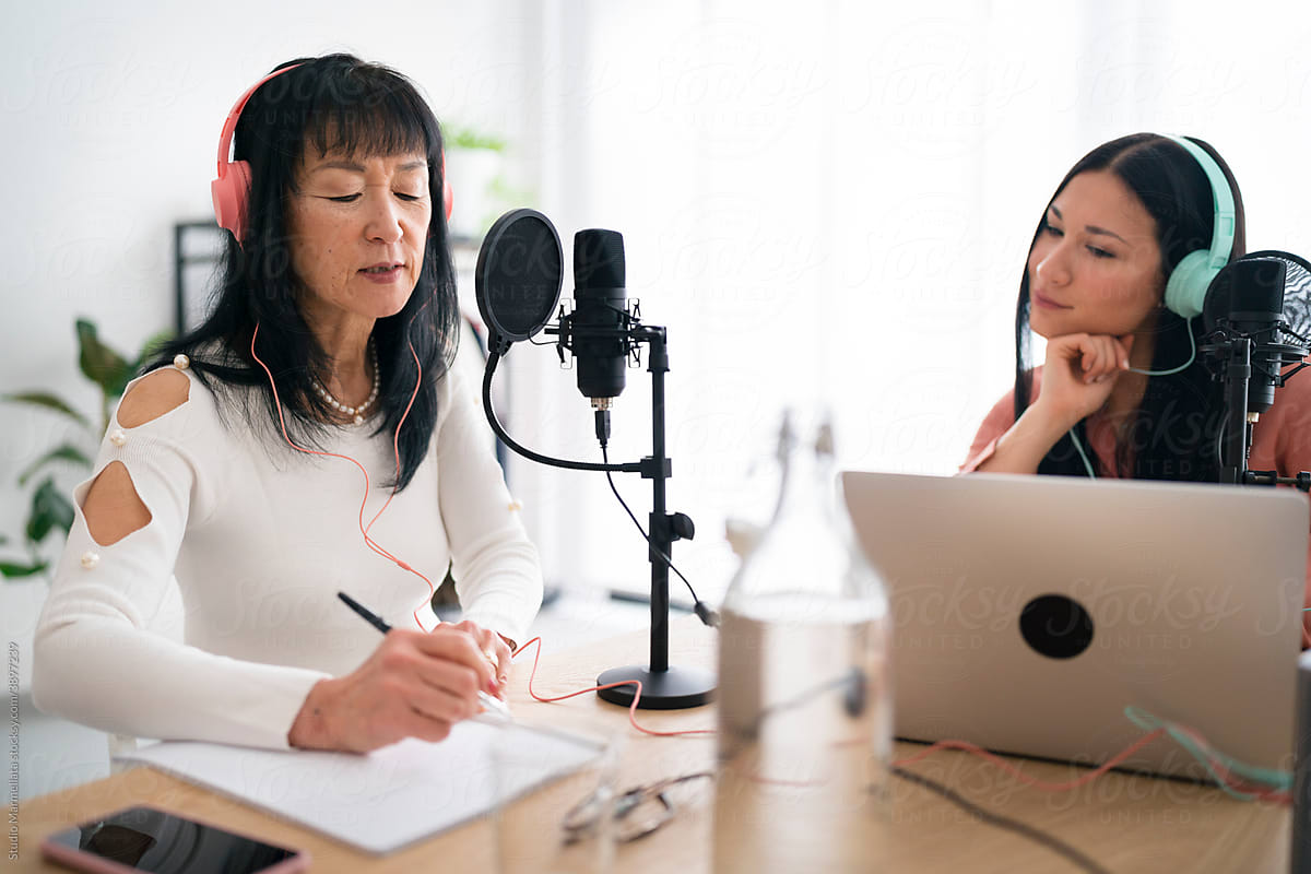 Asian female podcasters checking script before recording session