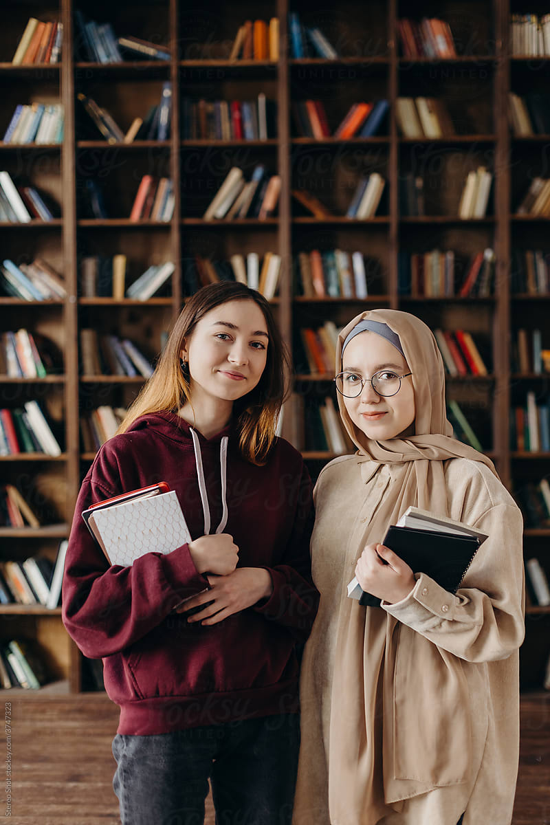 Content diverse female students with textbooks posing in library