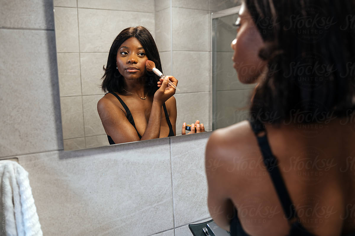 Black woman applying cosmetic product in bathroom