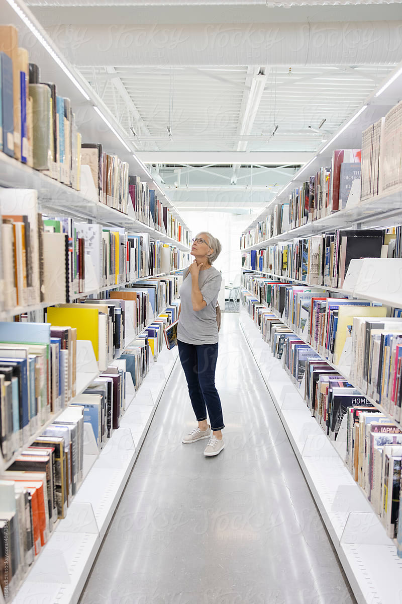 Senior woman looking for book on library bookshelf.