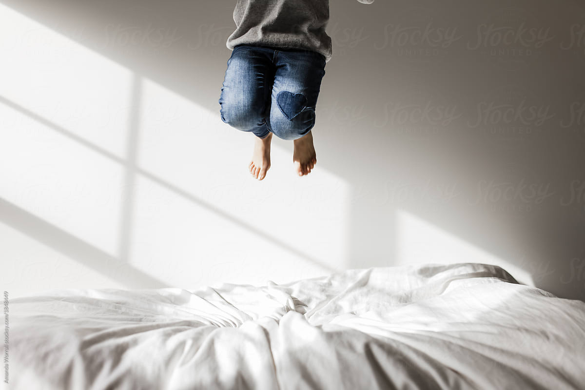 Girl with heart on her jeans jumping on a bed in an all white bedroom