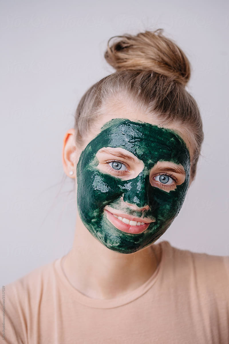 Lovely blond female with green skincare mask on her face