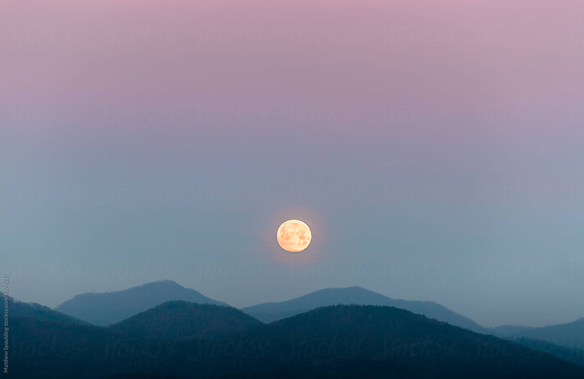 Moon setting into mountains under colorful sky