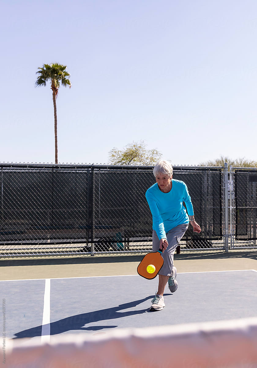 Senior Citizen Pickleball player on reaches to hit low ball