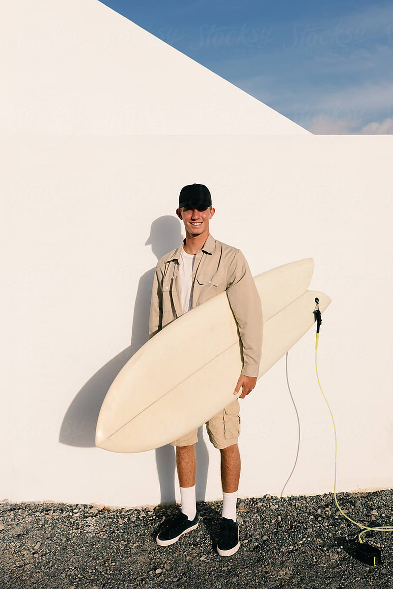 Professional surfer smiles at camera while posing against a white wall