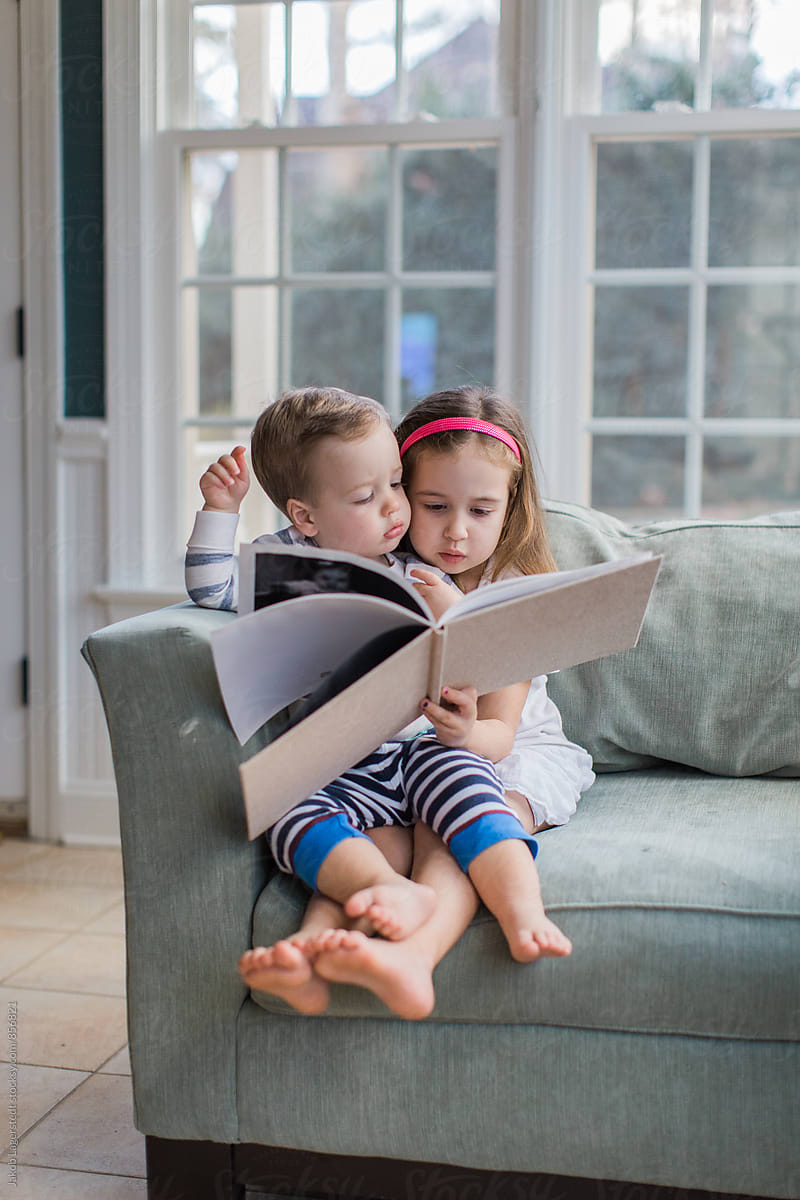 Young girl and boy toddler sitting on an oversized chair reading a book