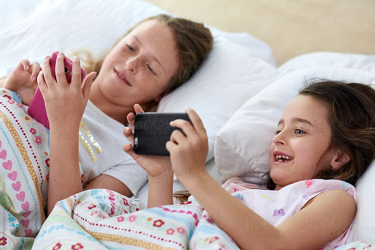 Siblings watching videos on digital devices in bedroom