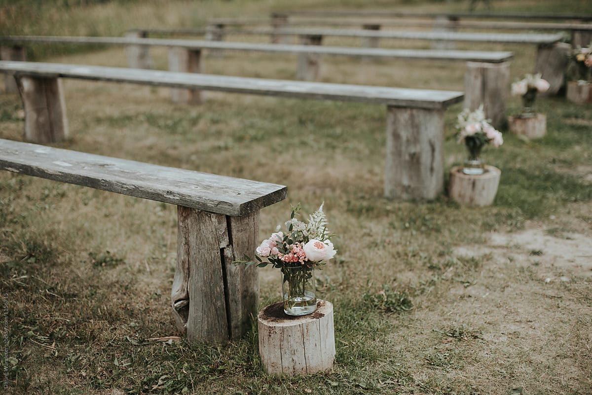 Simple outdoor wedding with wood stump benches for seating and simple flowers in mason jars