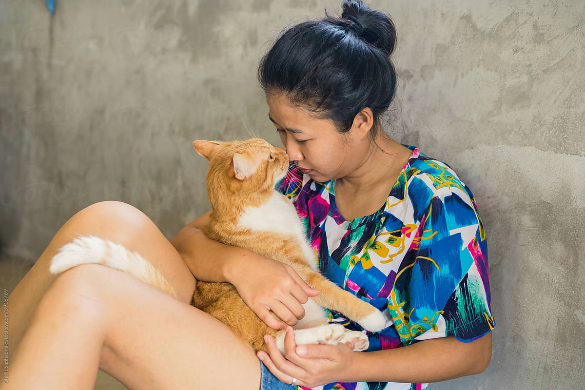 A sitting Asian woman hugging a cat