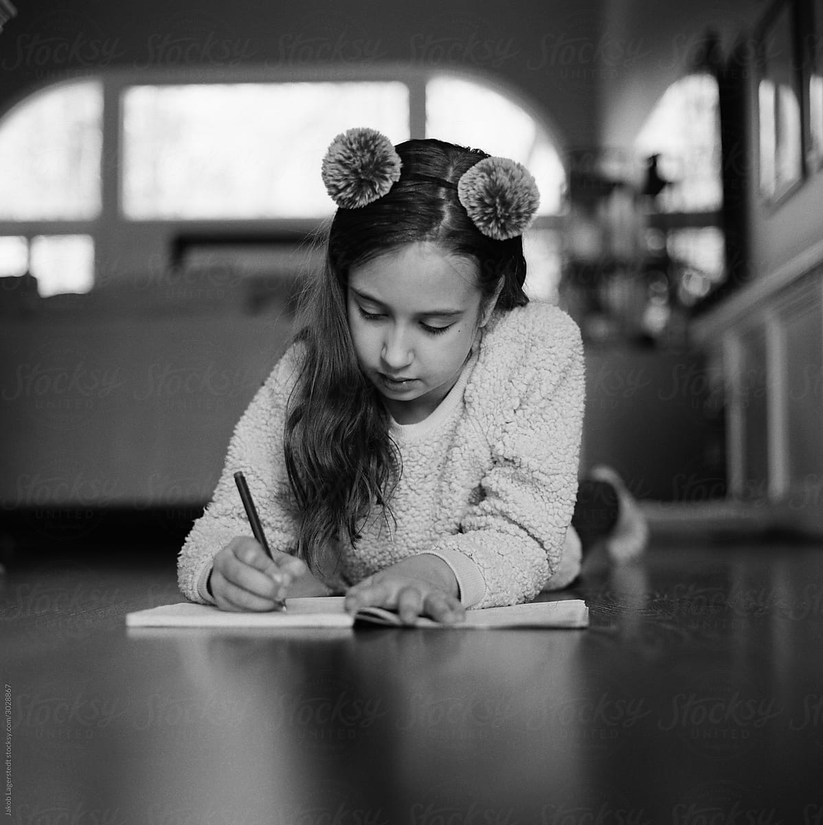 Young girl laying on a hardwood floor writing in a journal