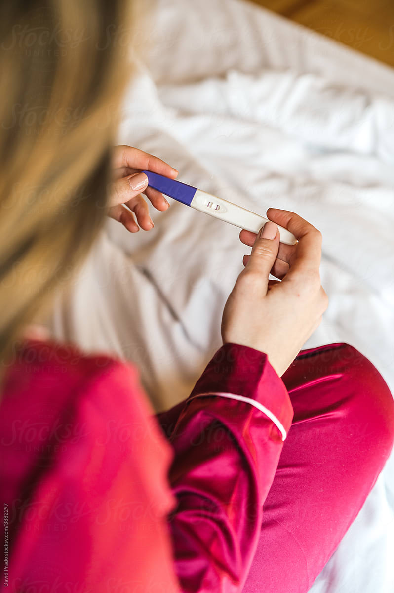 Woman with pregnancy test on bed