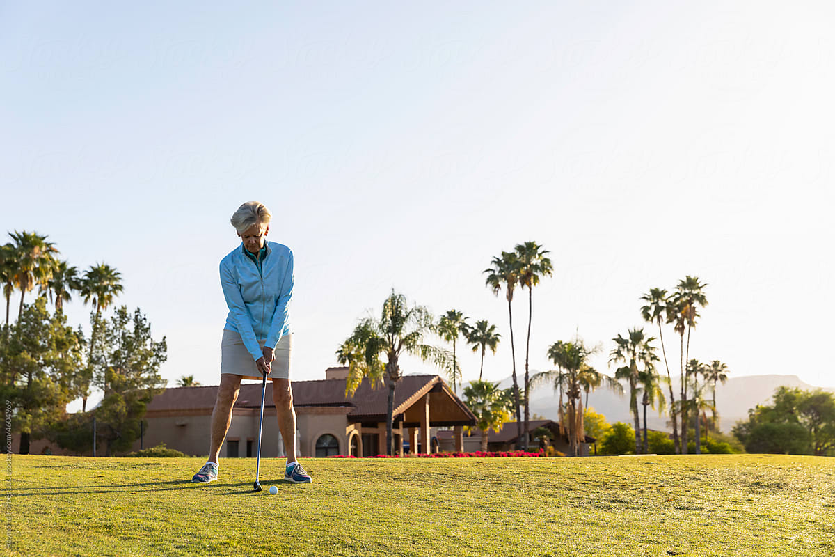 Healthy Senior Citizen Woman lines up golf shot on fairway