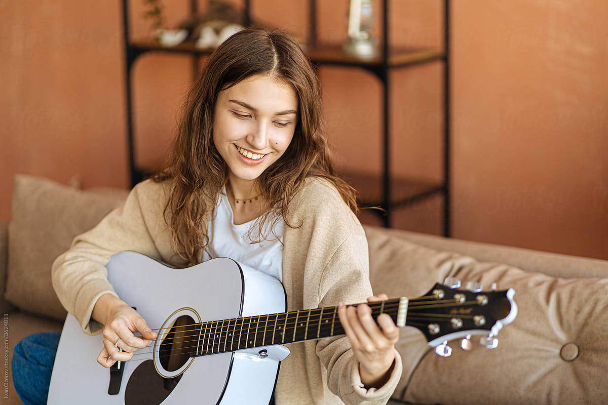 joyful young girl playing guitar while sitting on sofa