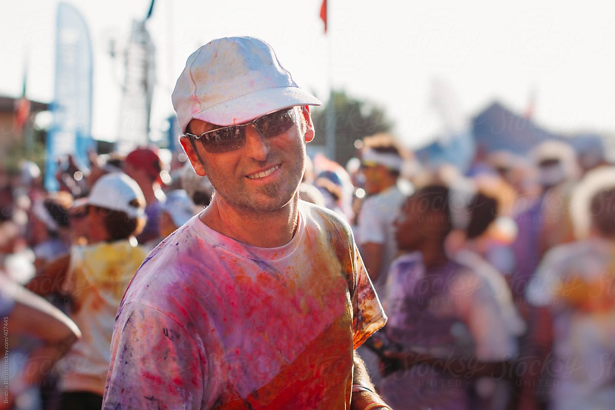 Man looking at camera, he is full of colors made by holi powder,unrecognisable people in background