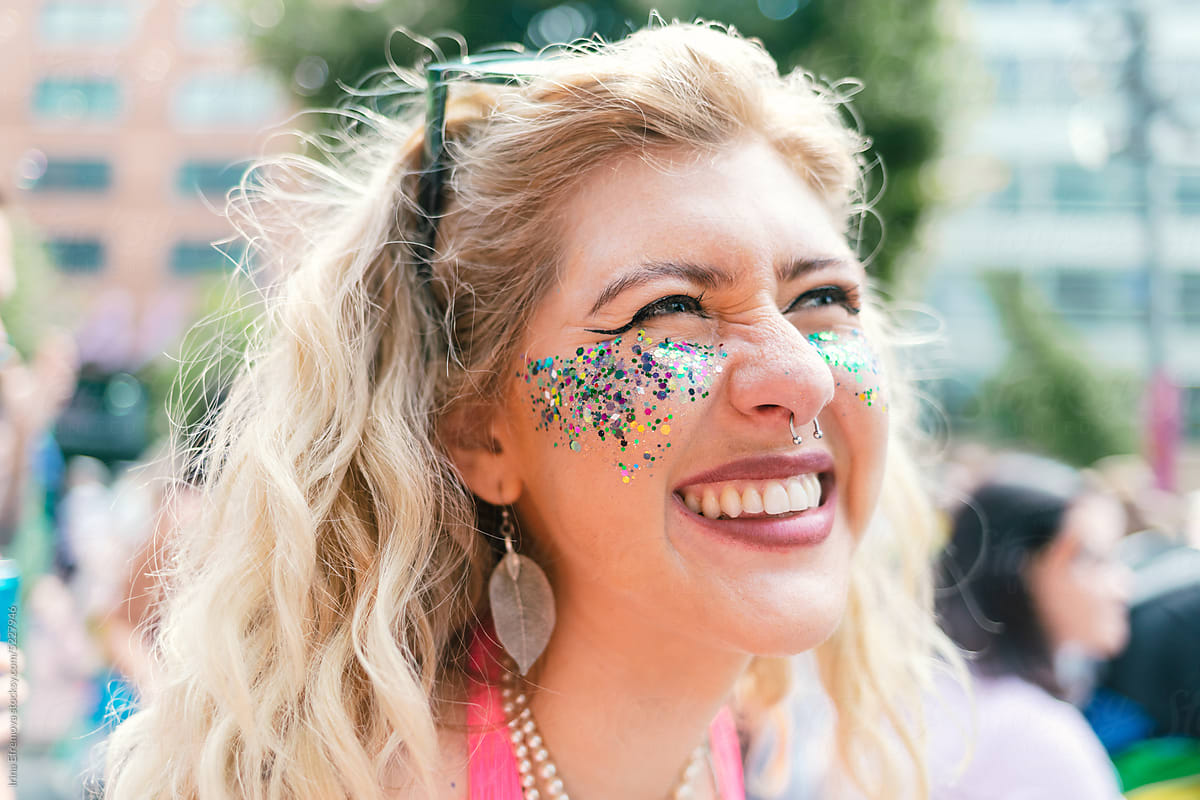 Curly blond Woman with glitter on her face at Pride laughing