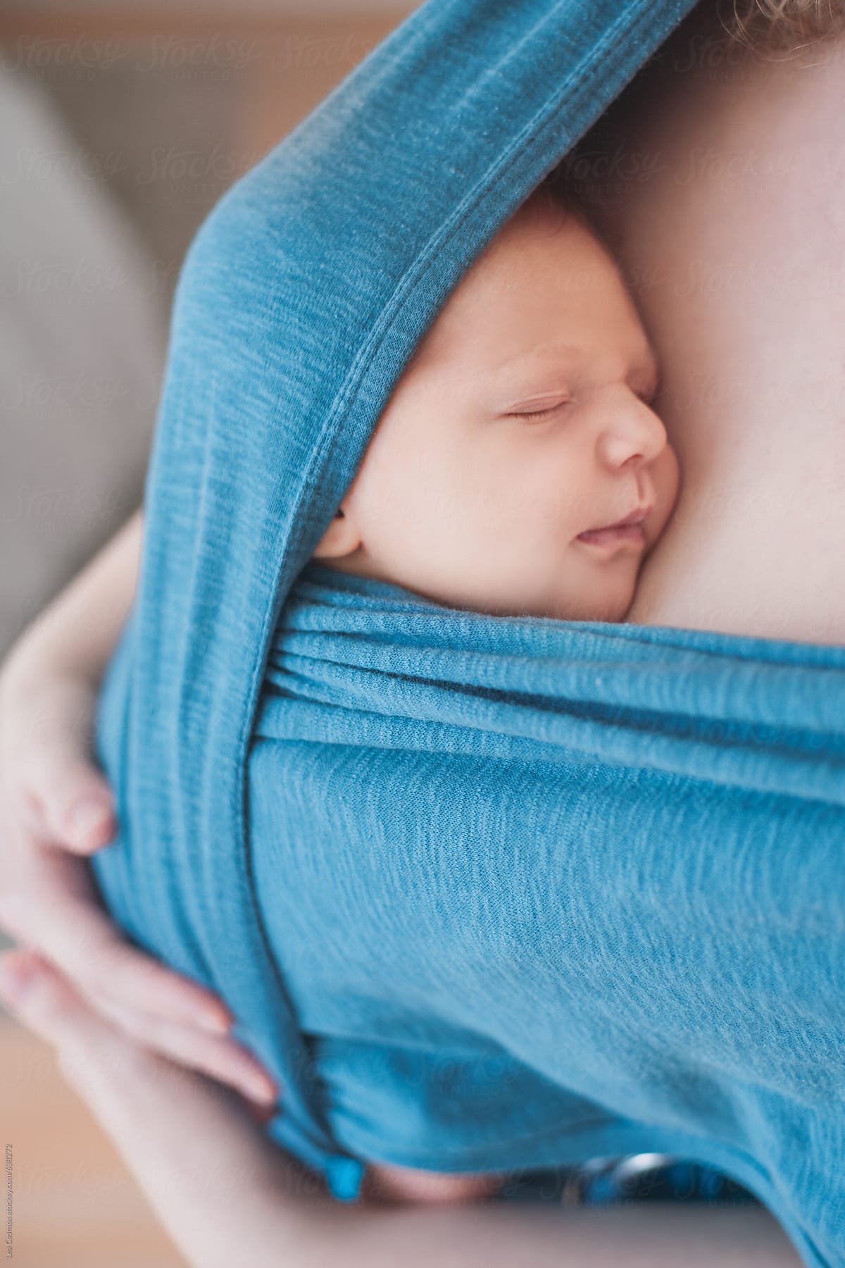 Newborn baby sleeping on his mother's chest wrapped up in a baby carrier