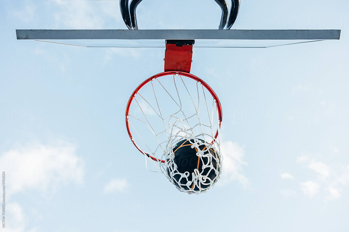Basketball scoring through the net against a sky backdrop