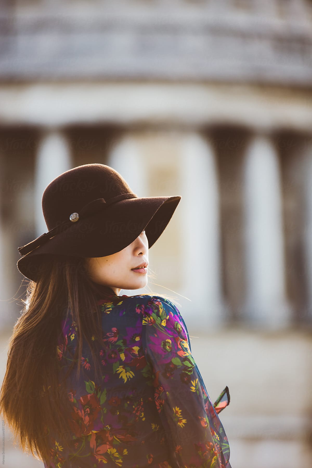 Profile of an asian girl wearing a floppy hat with a blurred building in the background