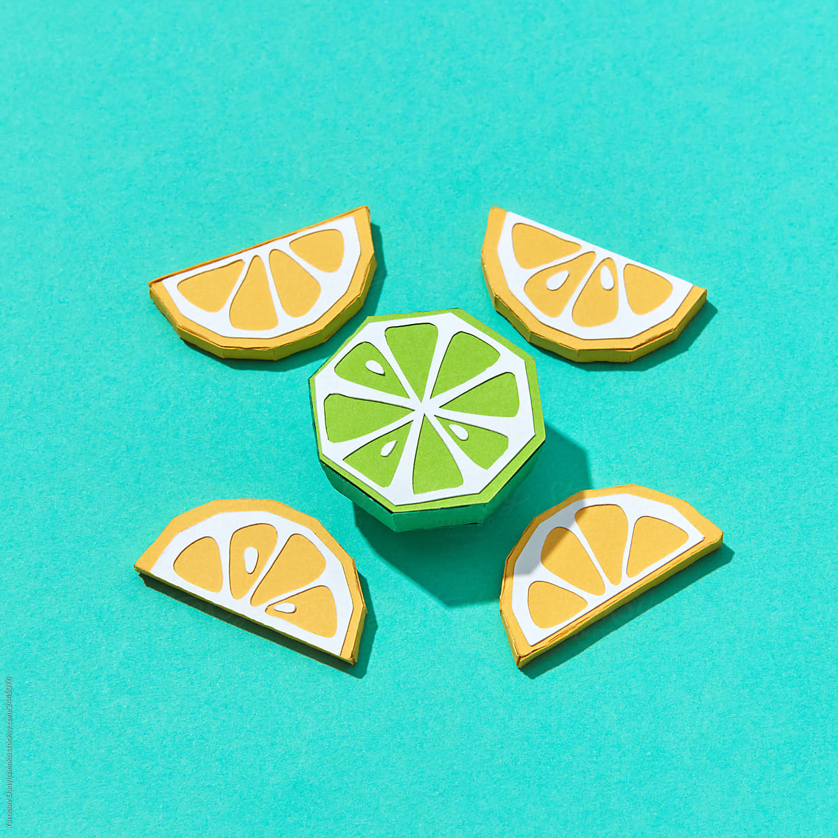 Paper handmade origami of lemon and lime slices on turquoise background.