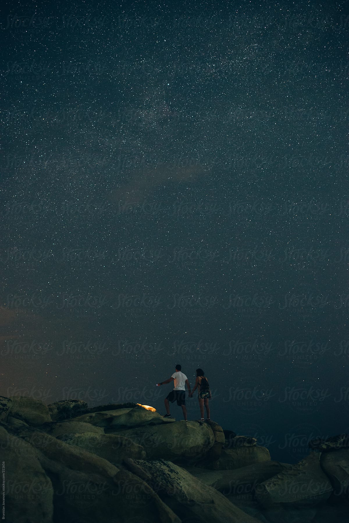 Couple exploring the rocky beach under the night sky