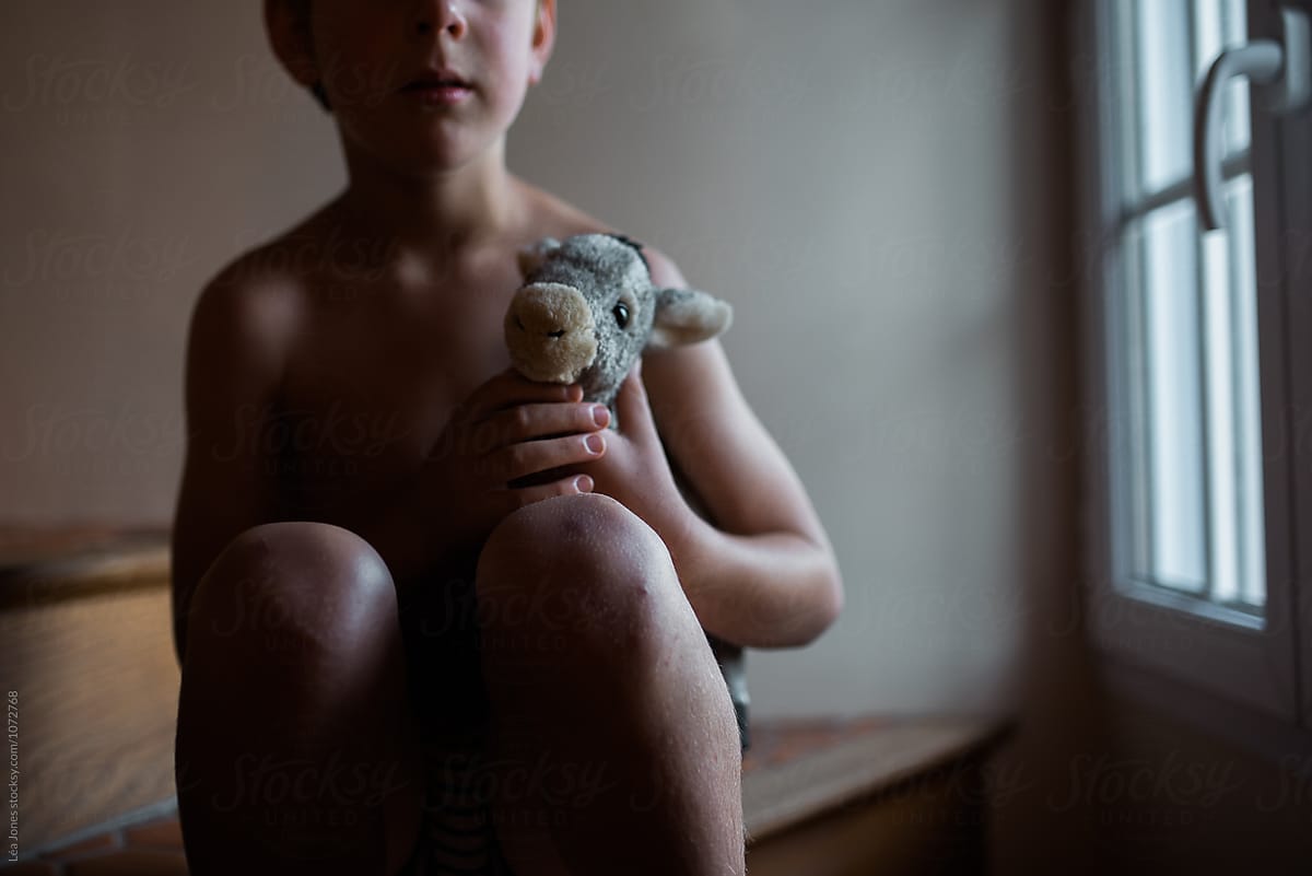 boy standing by window with stuffed donkey in hands