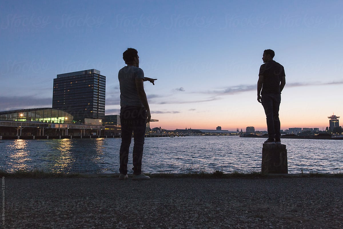 Two friends standing together at the waterfront, during senset or dusk