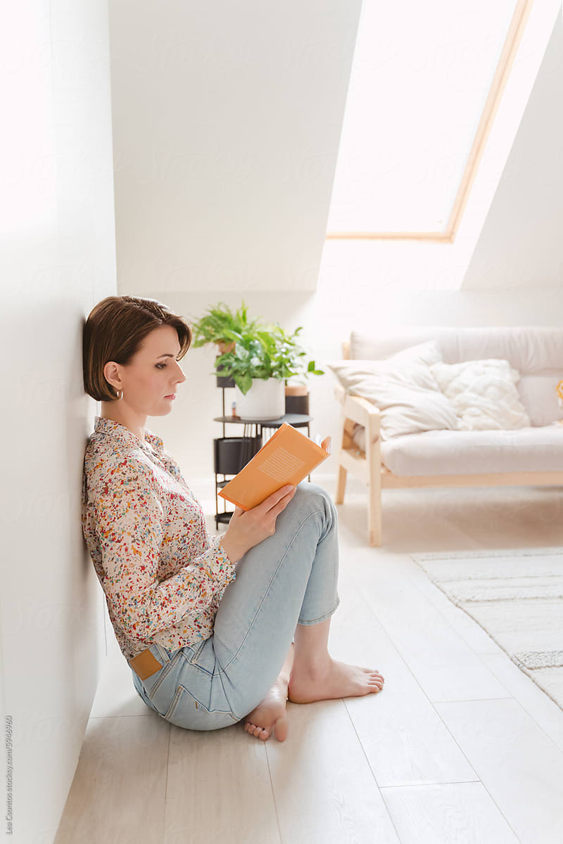 Young woman sitting on the floor in her bedroom and reading a book.