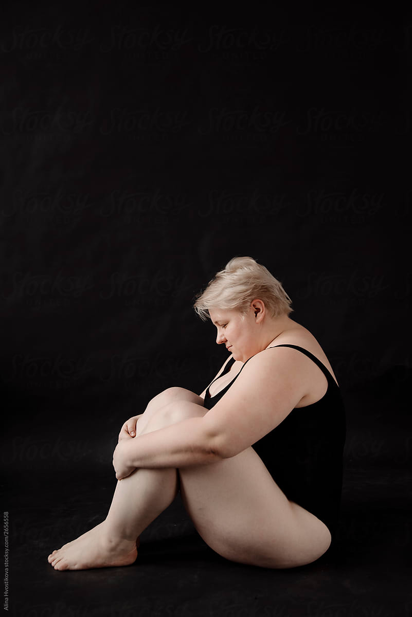 Sensuality woman sitting on floor, embracing legs.