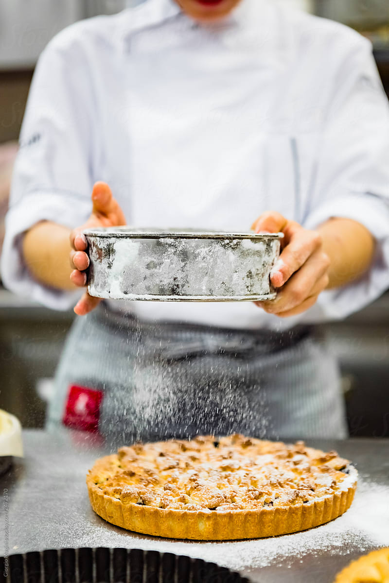 Pastry Chef Pouring Powdered Sugar on a Cake