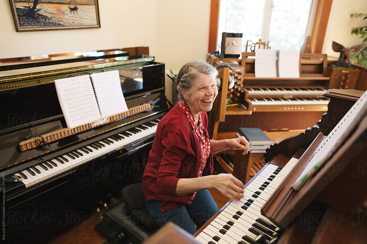 Happy mature woman playing piano and organ in home studio