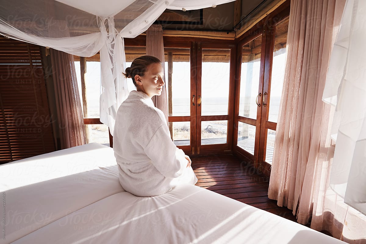 Young woman in a bathrobe watching the sunrise from her hotel bed