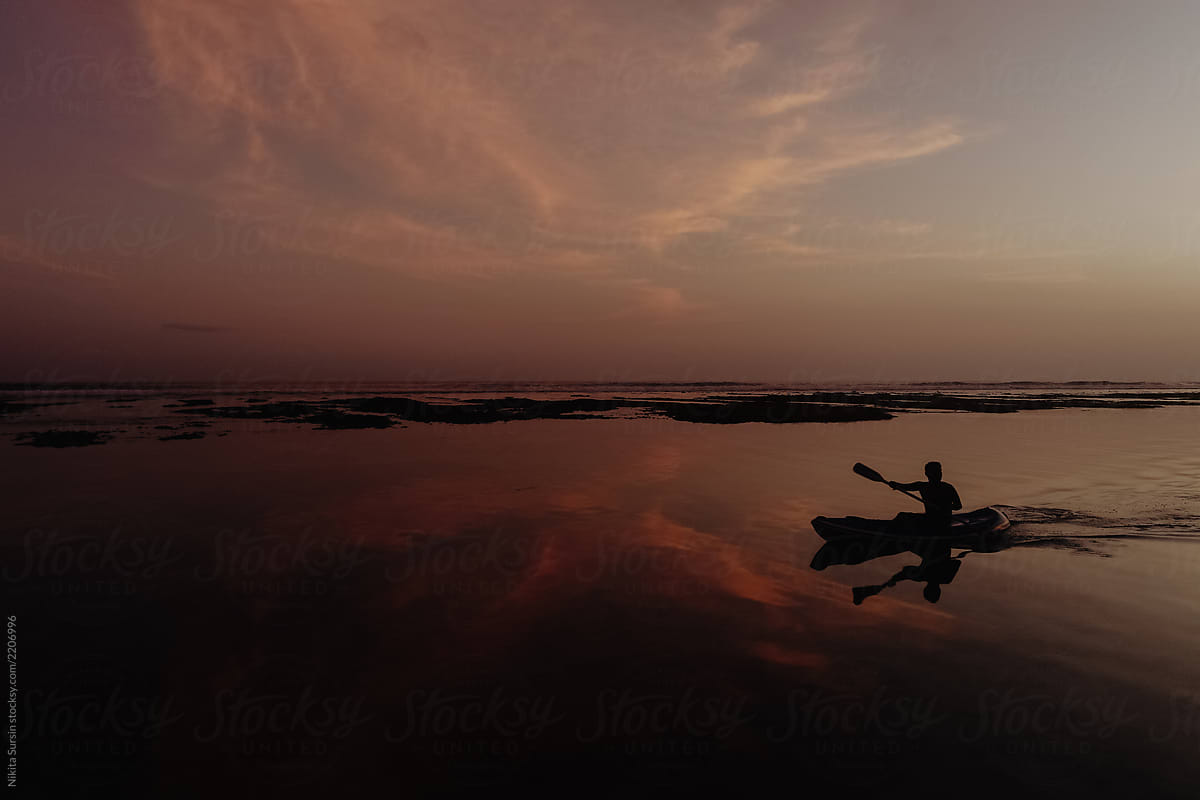 man swims in a canoe, paddles rowing. Beautiful sunset and low tide in the ocean