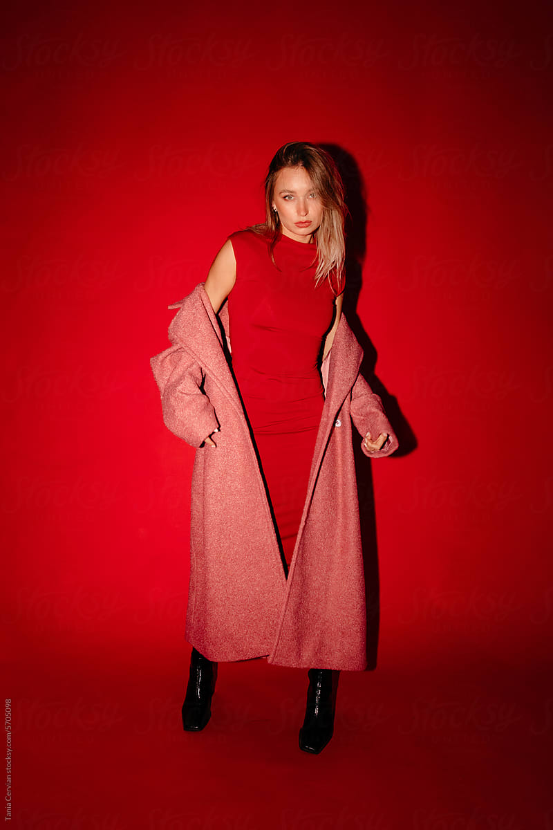 Stylish woman in red gown and coat standing in studio