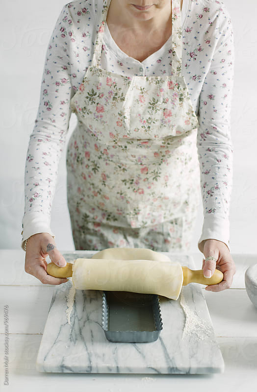 Woman preparing a lemon tart: Woman rolling pastry onto a tart tin.