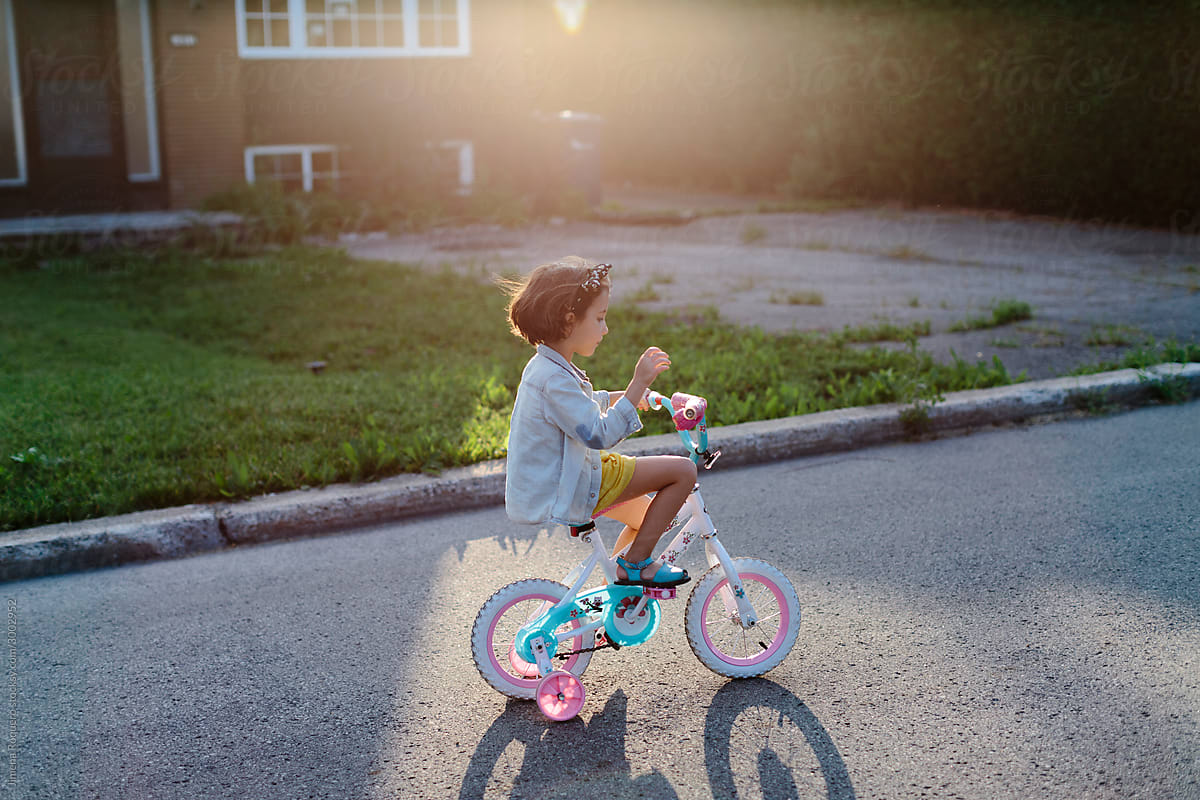 Little girl riding her bike in sunlight in the suburbs