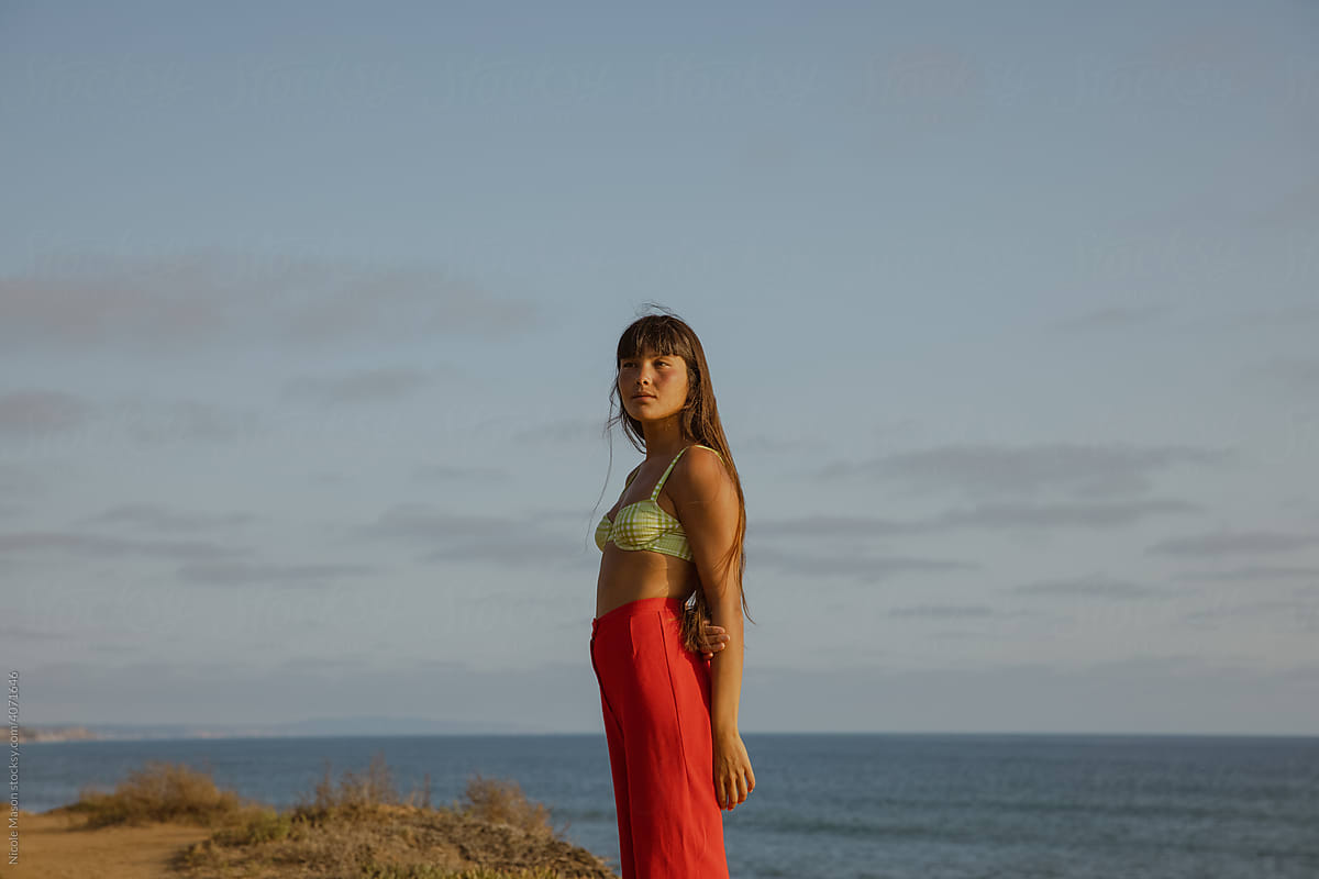 woman in red pants standing on cliff by the sea