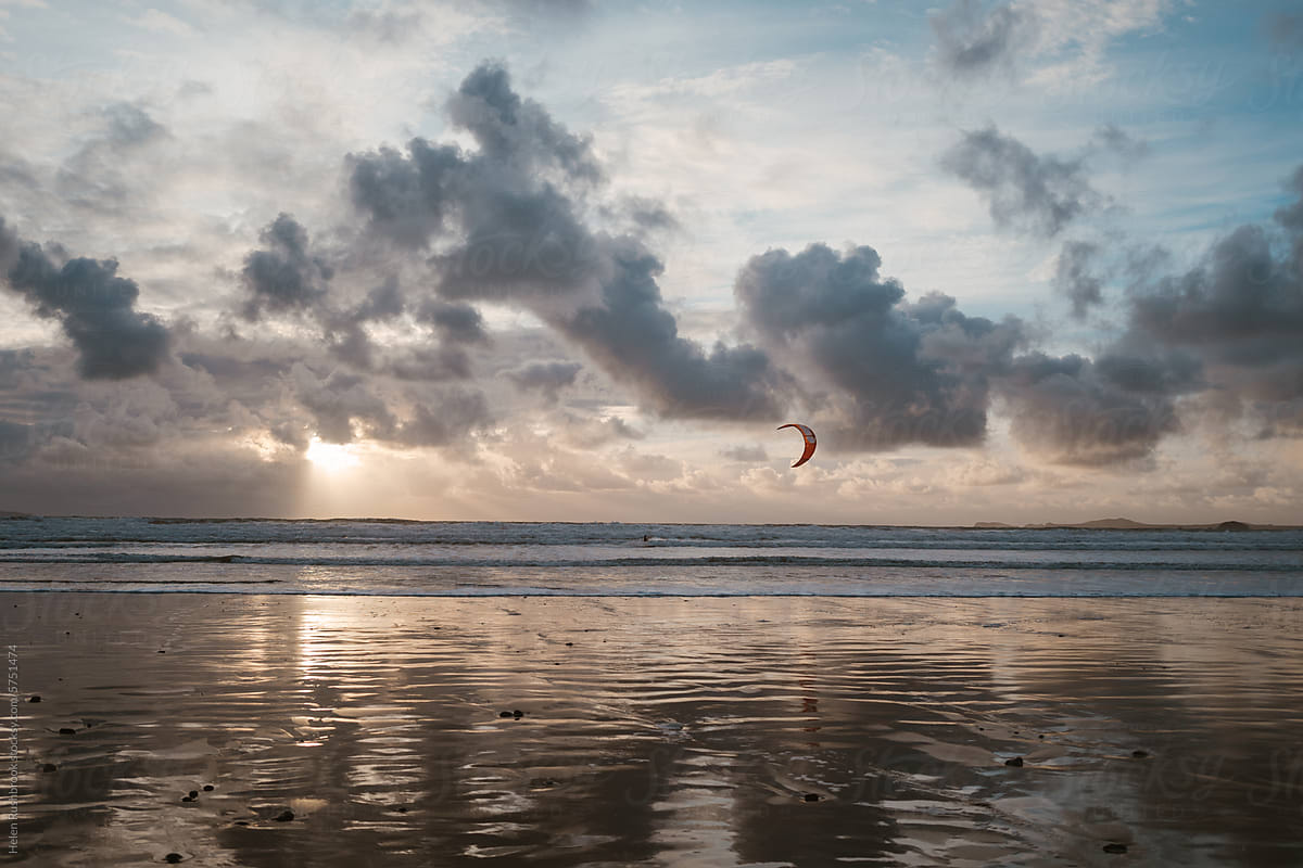 Sunset cloudy beach scene with anonymous kite surfer.