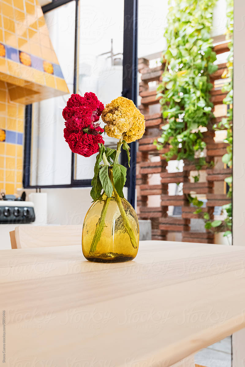 A glass vase with flowers on a wooden table in a kitchen