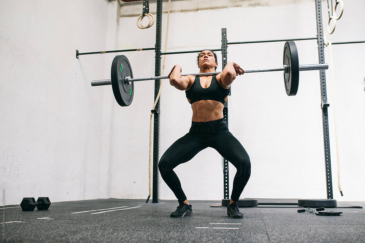 Hispanic female weightlifter squatting with barbell