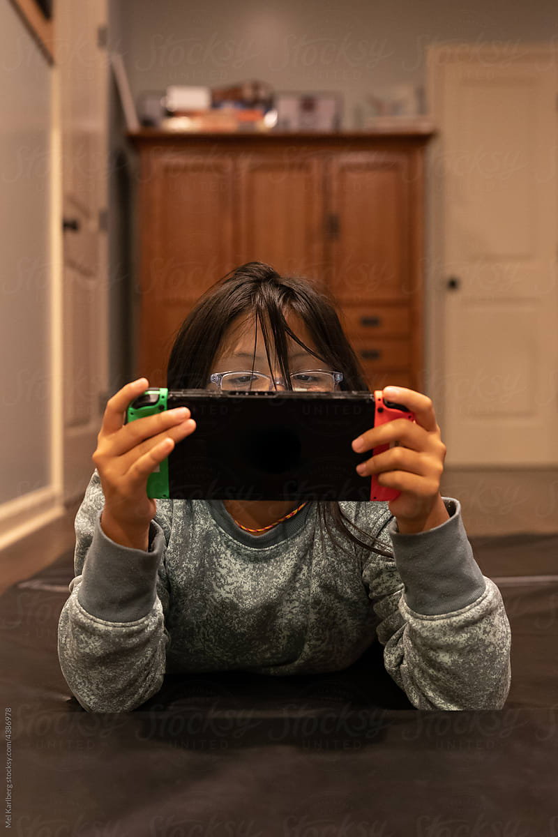 Girl lying on floor playing handheld gaming system