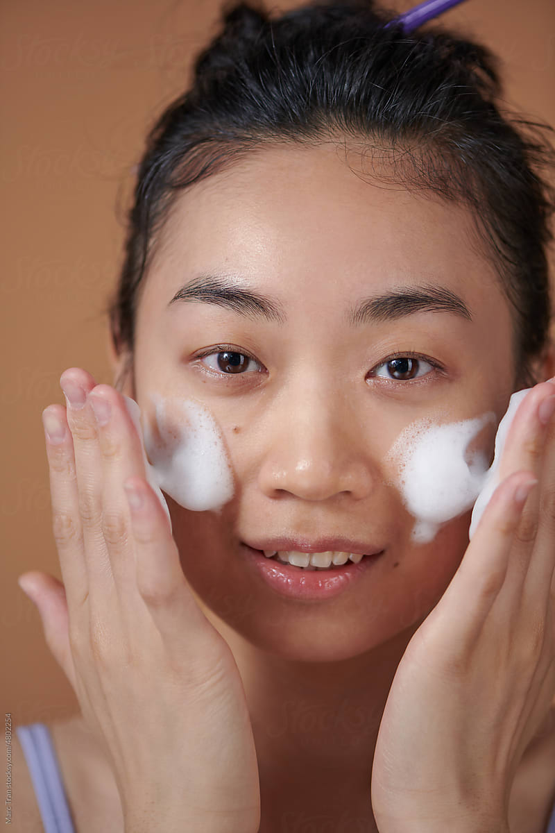 Smiling young woman washing foam face by natural foamy gel.