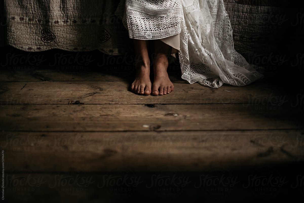 Unrecognizable bride in white dress standing barefoot in house