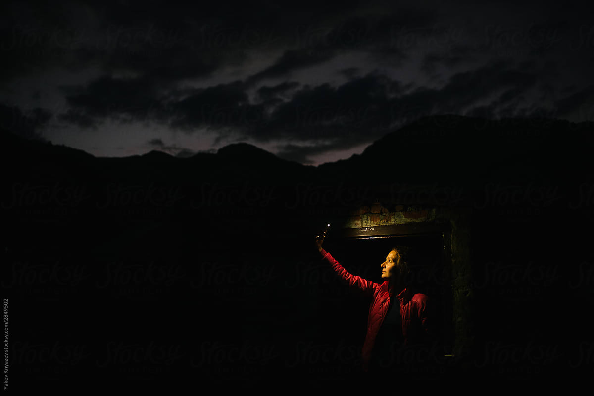 Young woman in the door frame of a roof outbuilding at night lit by the smartphone screen