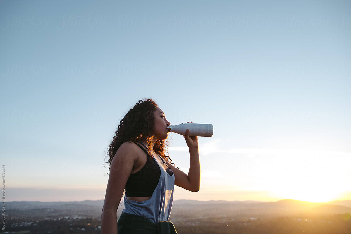 Teenage girl drinking from water bottle at sunset.